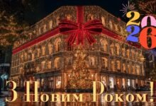 Святкова листівка 2026 року з нічним містом, будівлею, обгорнутою гірляндами й червоною стрічкою, та феєрверками навколо цифр 2026.