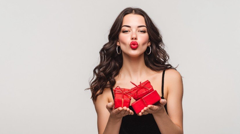 Молода жінка тримає в руках святкові подарунки та посилає повітряний поцілунок — святковий настрій для привітань племінниці від тітки.