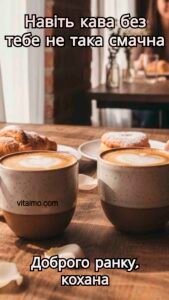 Дві чашки кави з молочною пінкою у формі сердець та круасани на дерев’яному столі в затишній кав’ярні.