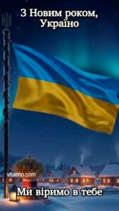 Український прапор на щоглі з тризубом, що майорить над засніженим селом у зимову ніч із написом З Новим роком, Україно. Ми віримо в тебе