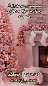 Новорічна листівка для коханої з рожевою засніженою ялинкою біля каміна, гірляндою та новорічними панчохами.