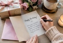 Writing a personal birthday message in a greeting card with flowers, gift, candle and coffee